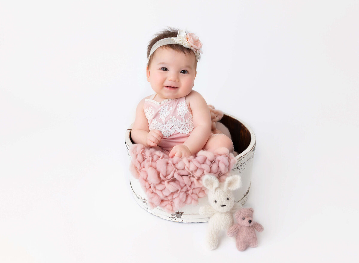 Baby girl 6 months old posing in white busket sitting and smiling during baby photography photoshoot in Brooklyn,  NYC