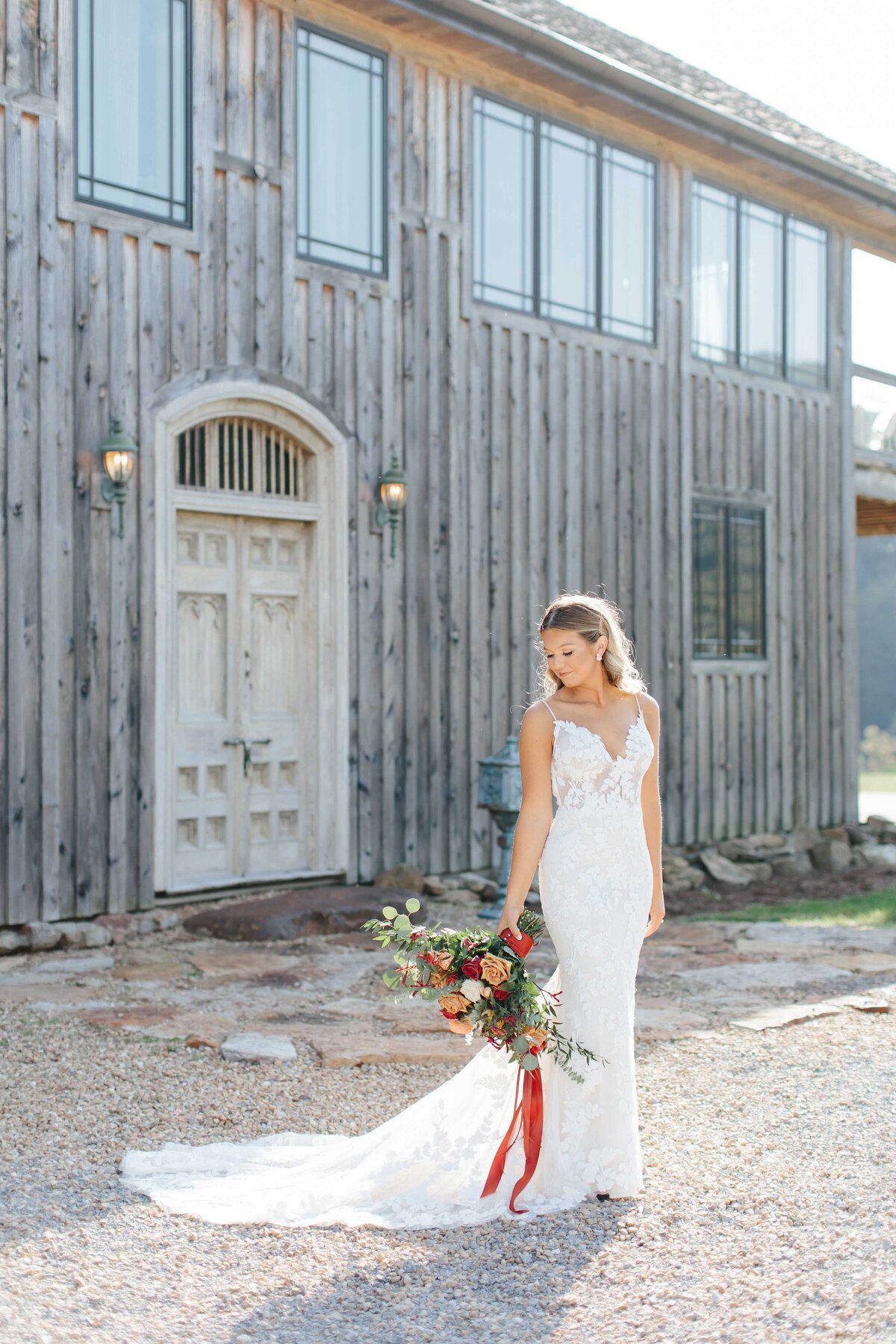 bride holding flowers to the side with crooked river wedding venue tobacco  barn in background
