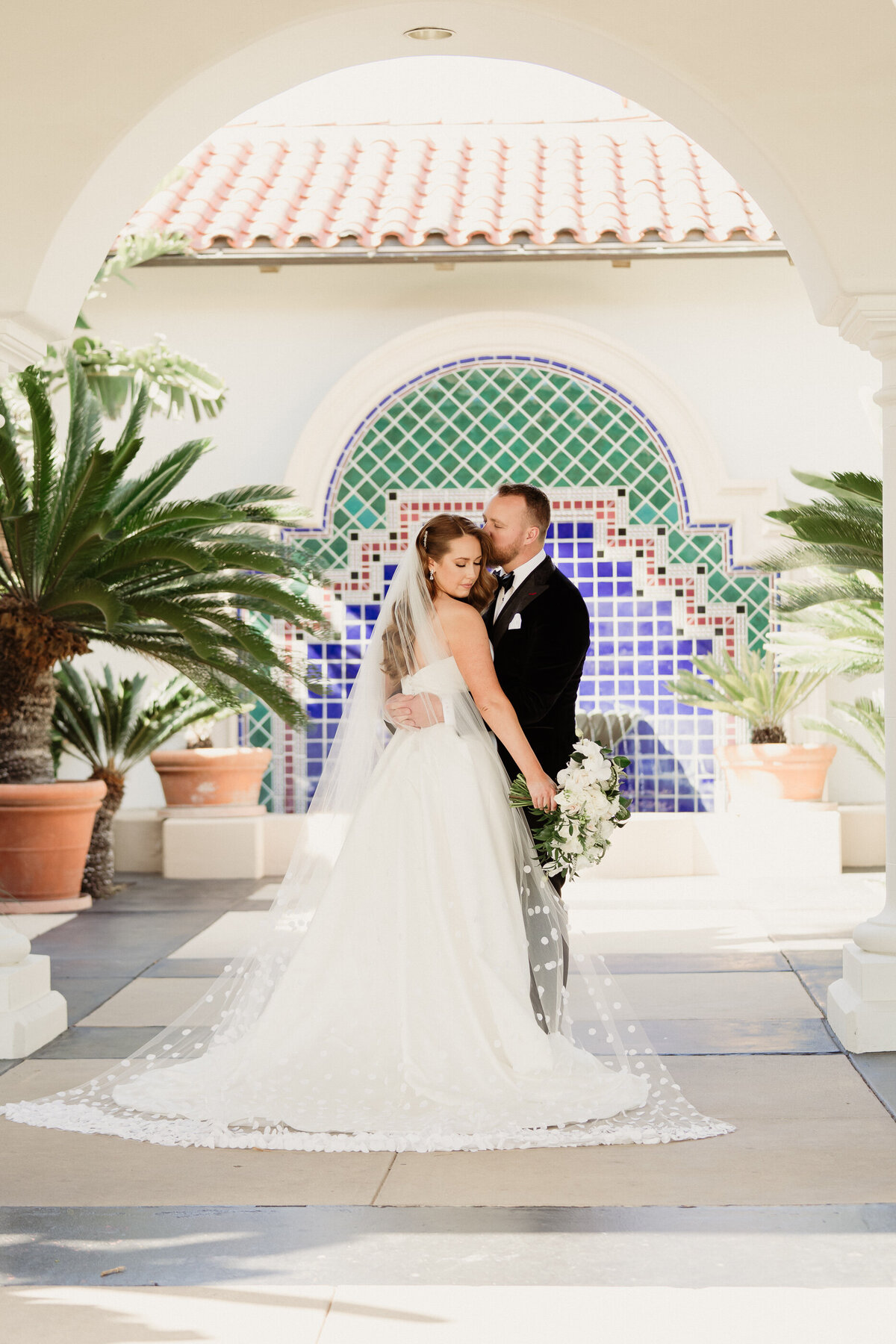 bride in a cathedral polka dot veil with a large white bouquet and groom in a black tux with a bowtie kissing during romantics at spanish hills country club captured by los angeles wedding photographer magnolia west photography