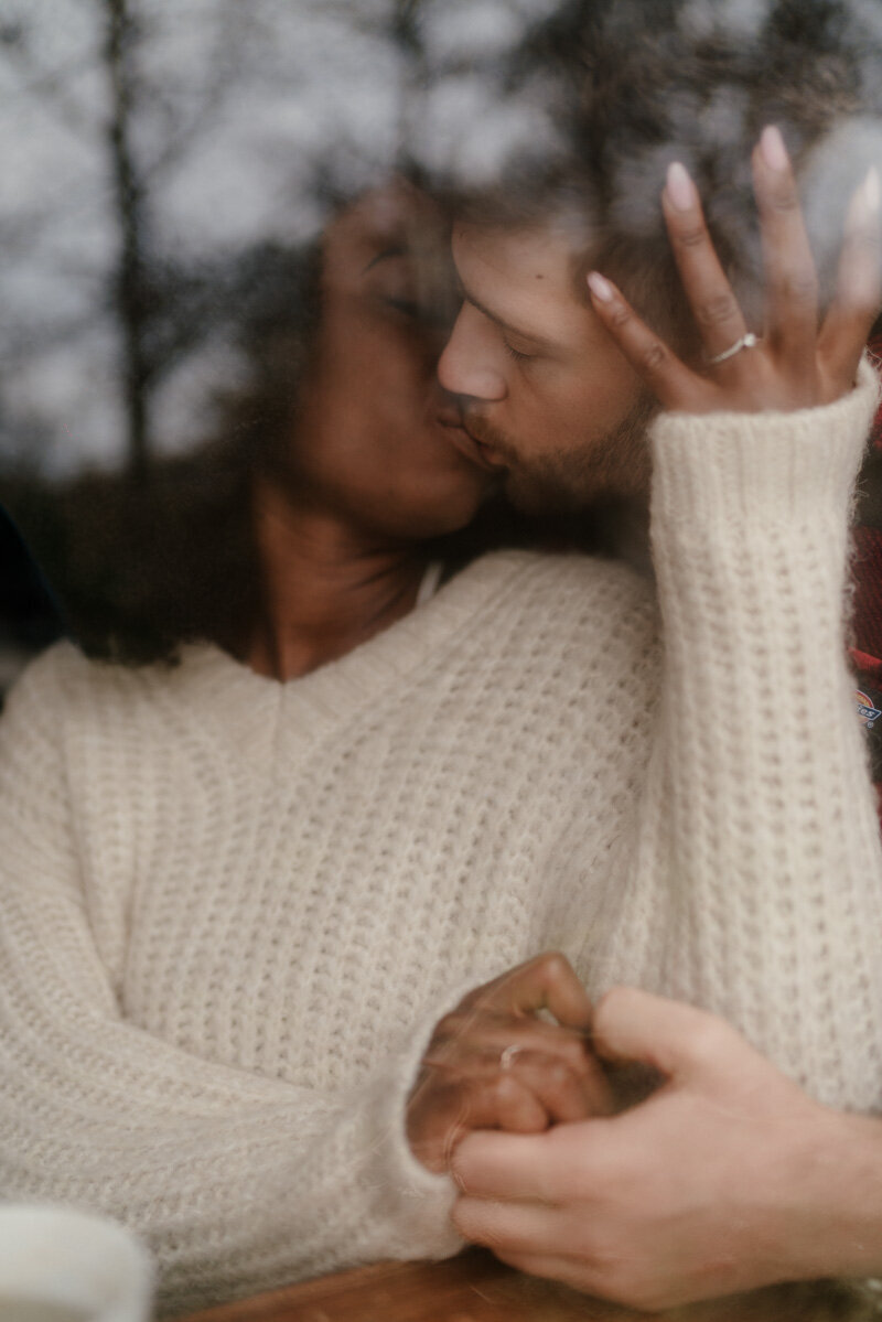 Séance photo sur l’île de Skye, couple s’embrassant à travers une vitre, reflet poétique et douceur écossaise.