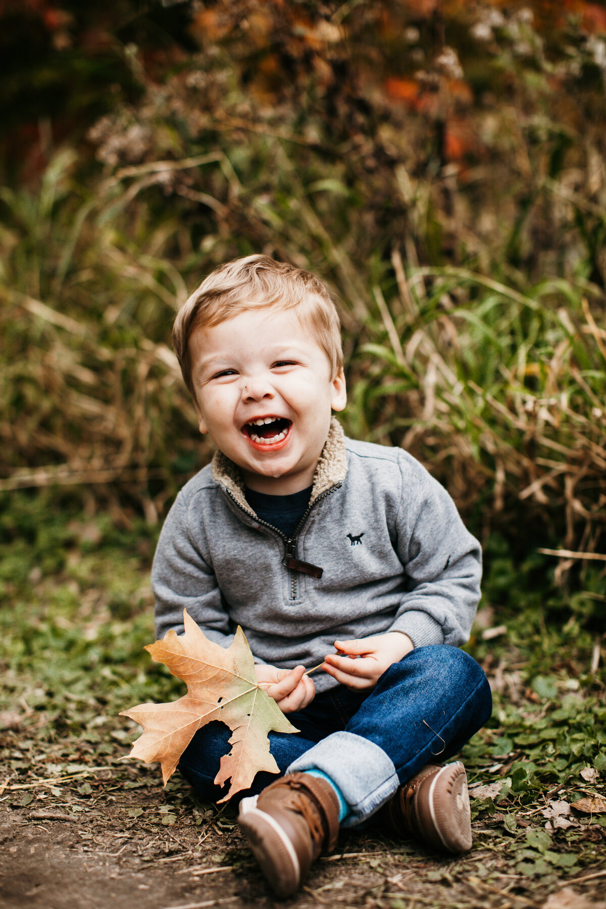 little boy sitting on ground laughing playing in leaves