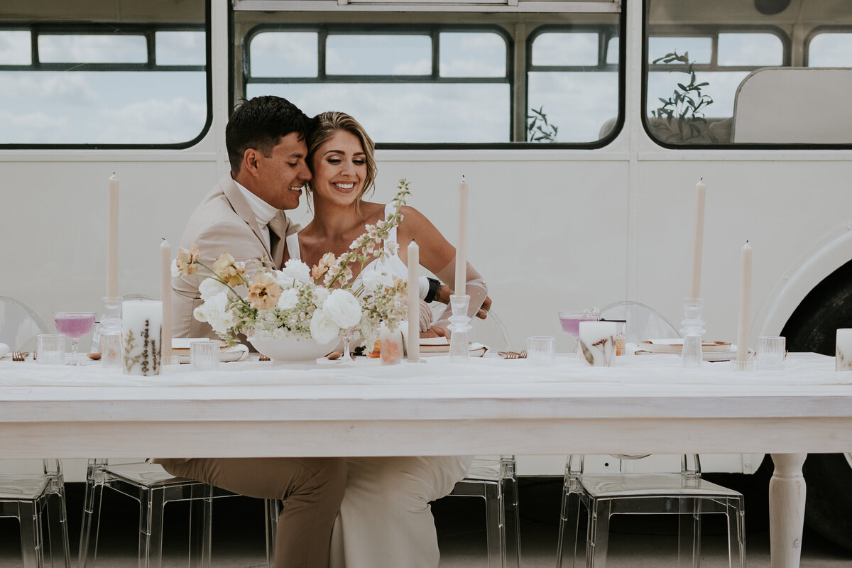Bride leans into groom smiling while they sit at head table.