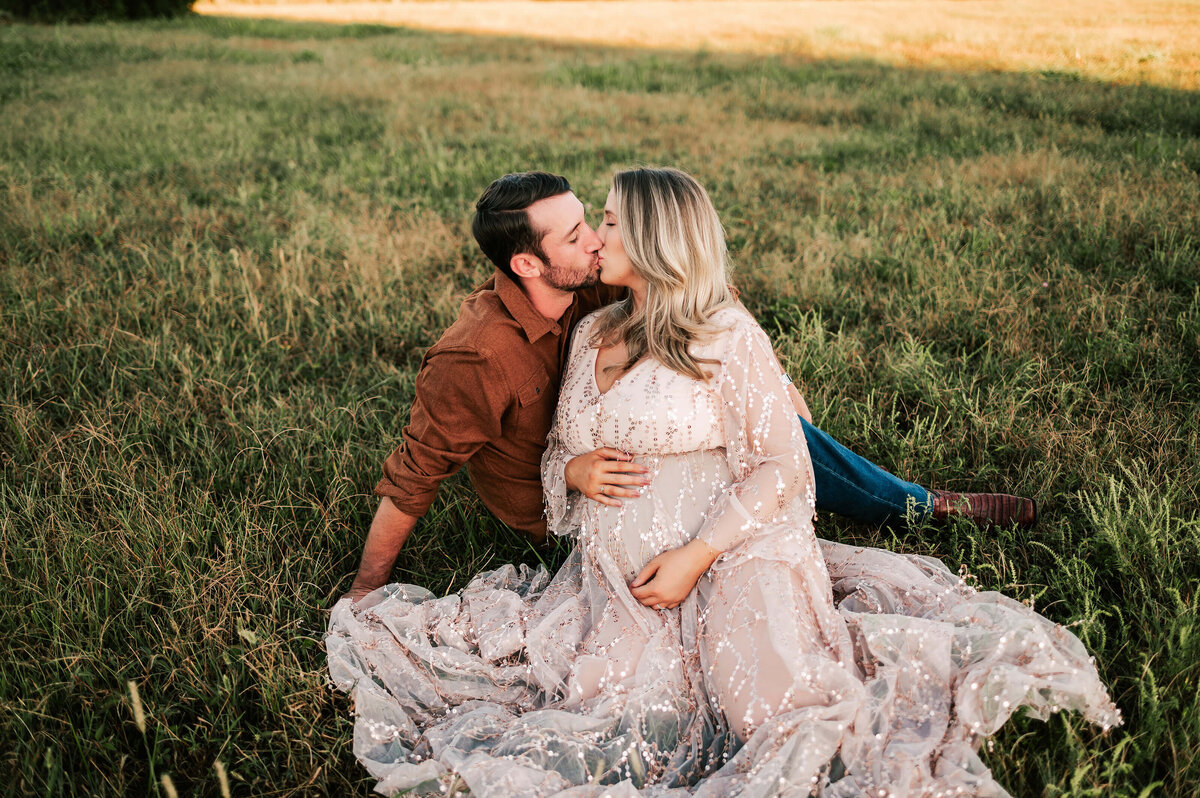 couple kissing holding baby bump in a field in Springfield MO