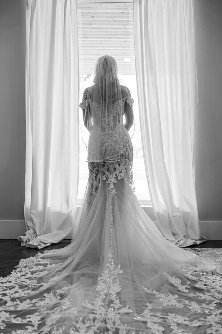B&W of the back of the bride in her dress staring out the window. Captured at The Venue at Oakdale in North Little Rock, AR.