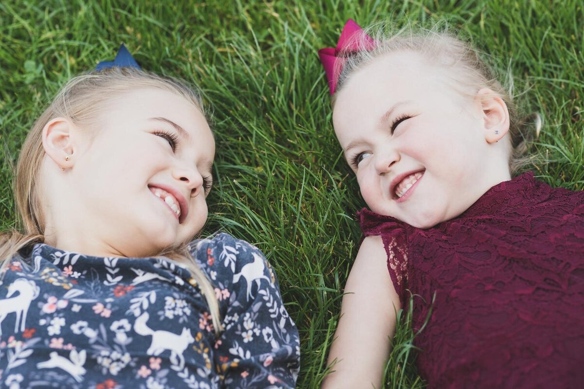sisters in grass smiling at each other