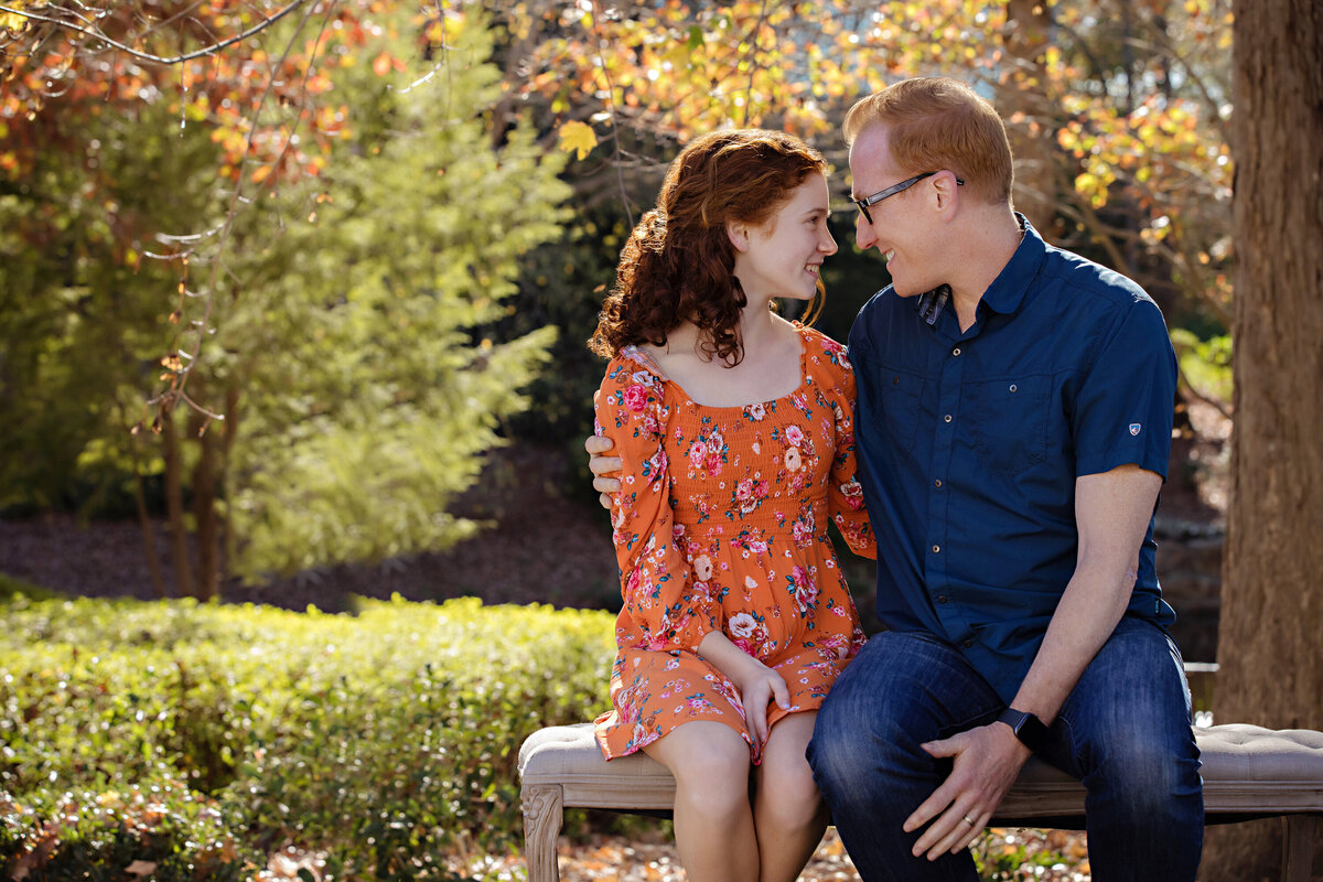 Heartwarming autumn portrait of dad and teen daughter on a park bench framed by colorful foliage at Ballantyne Corporate Park