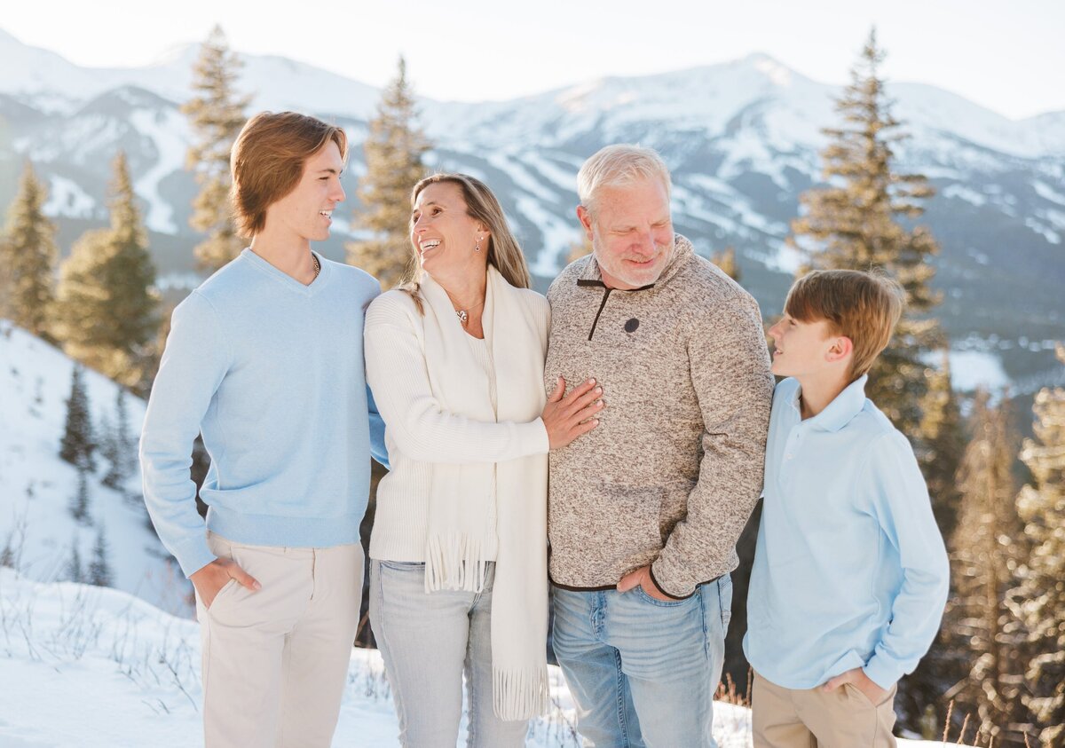 Teen brothers laugh with mom and dad on a snowy mountain overlook
