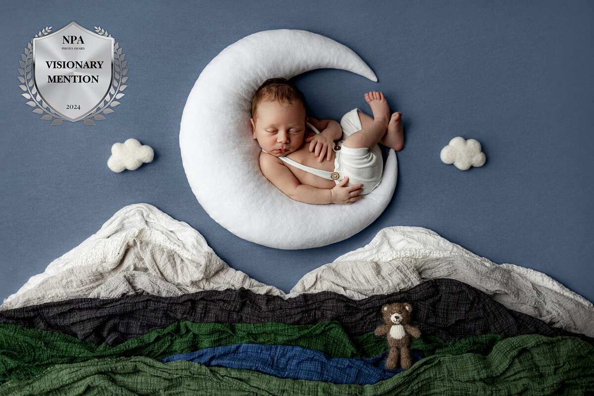 artistic photo of newborn sleeping on the moon above the mountains in petoskey mi