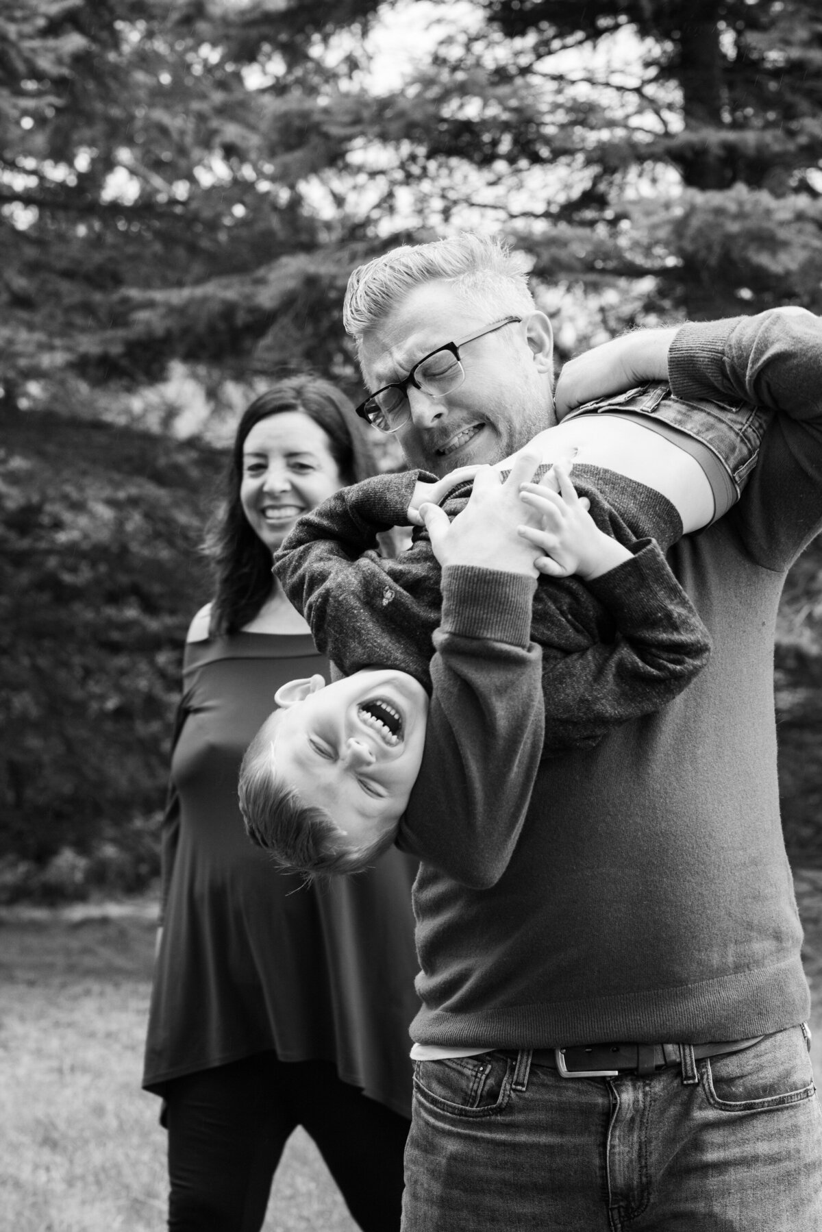 A parent holding their child upside down as they laugh and their other parent smiles from behind
