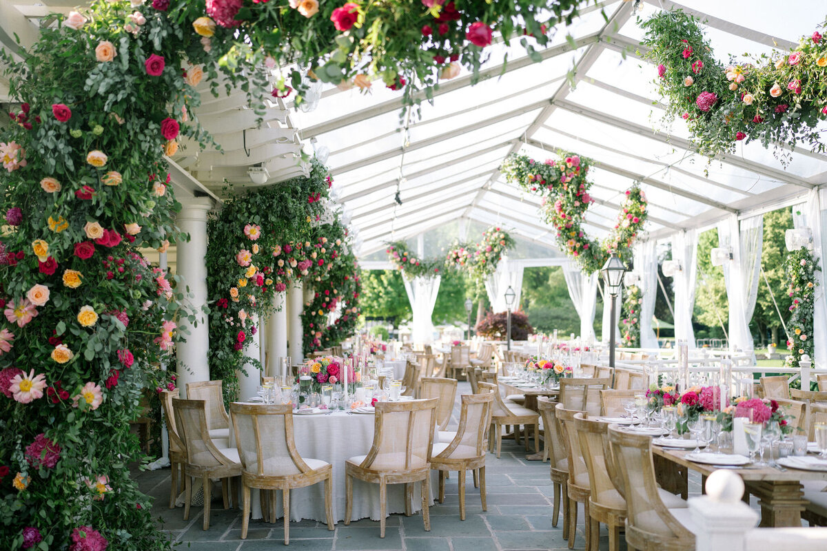 A spacious wedding dining area under a floral-decorated white canopy at Saddle Country Club, ready for guests.