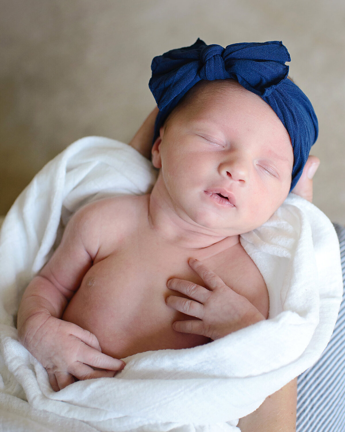 Sleeping newborn wrapped in a white blanket wearing a blue headband.