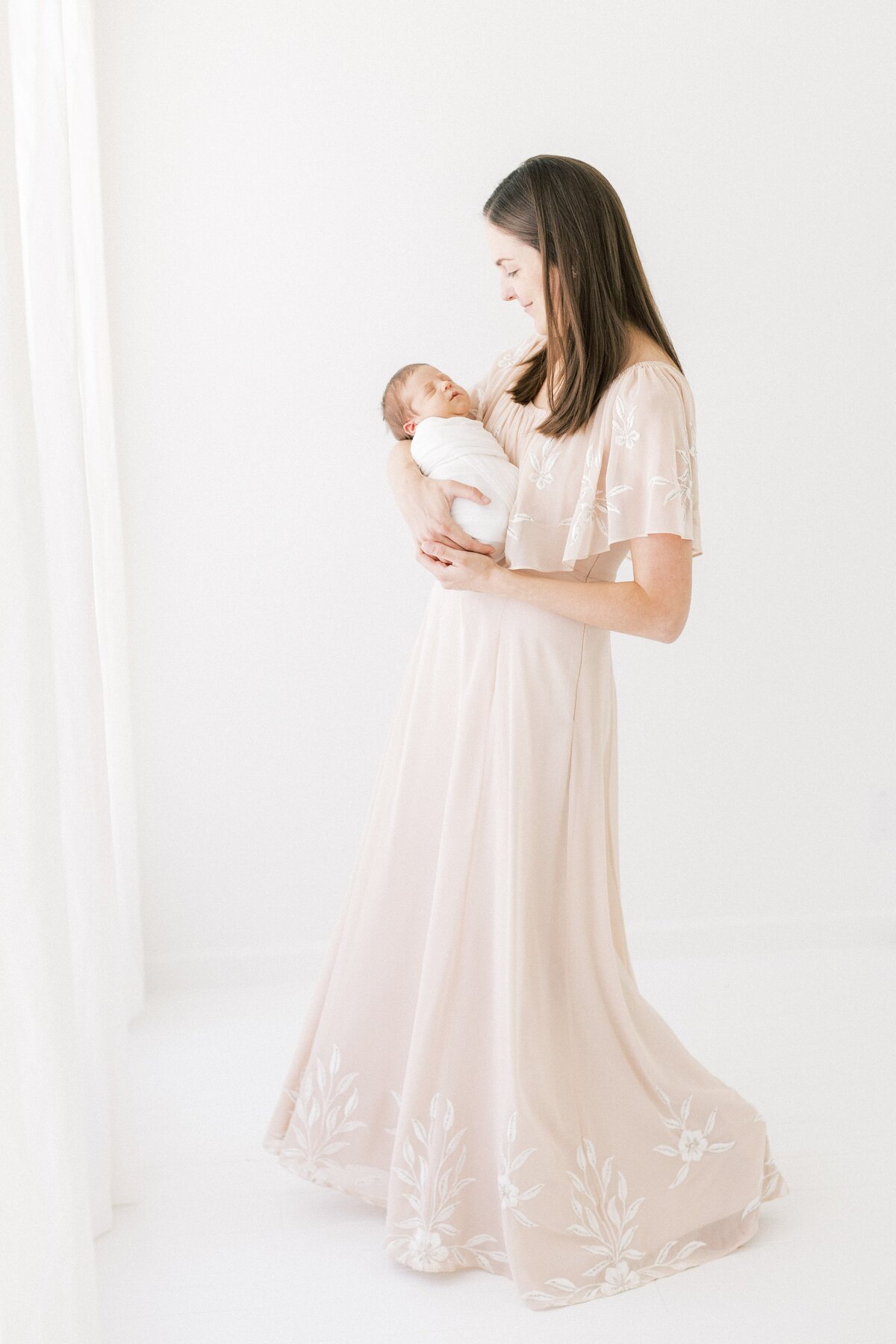beautiful mother standing and swaying rocking  her newborn baby to sleep wearing a long pink dress at her dallas newborn photography session
