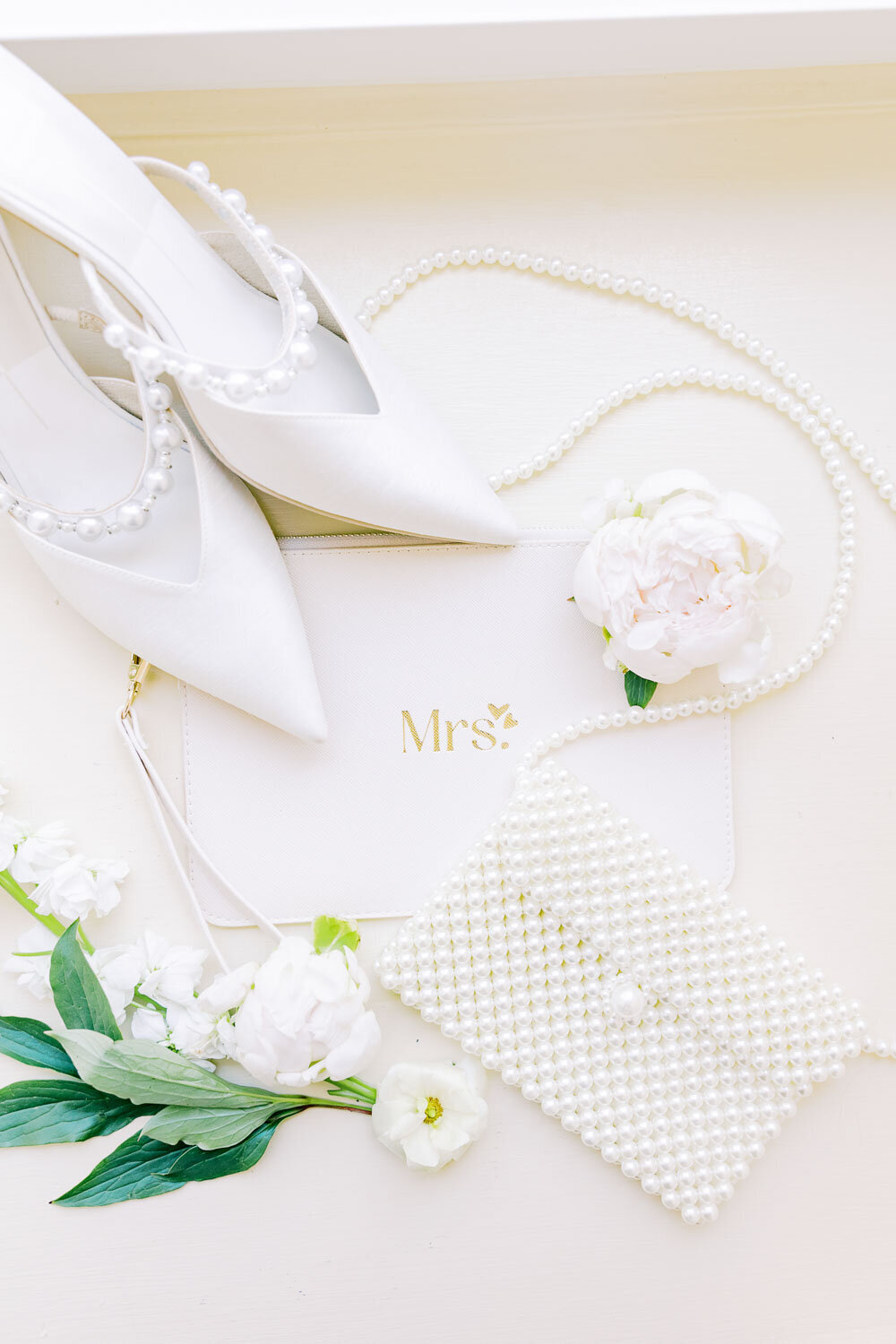Flat lay of bridal shoes, pearls, and Mrs. clutch