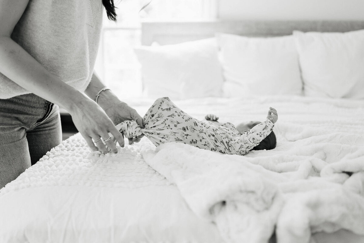 Close-up of a mother gently wrapping her newborn in a floral swaddle on a soft bed in Cleveland.