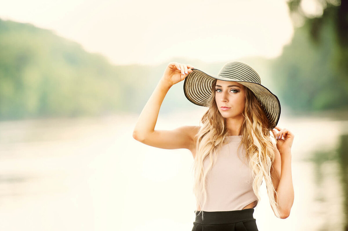 high school senior photo with sunhat on the side of river