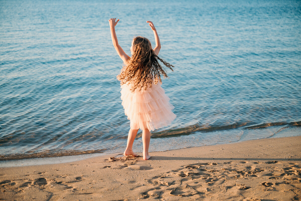 A girl dances on Carlsbad state beach while taking family photos