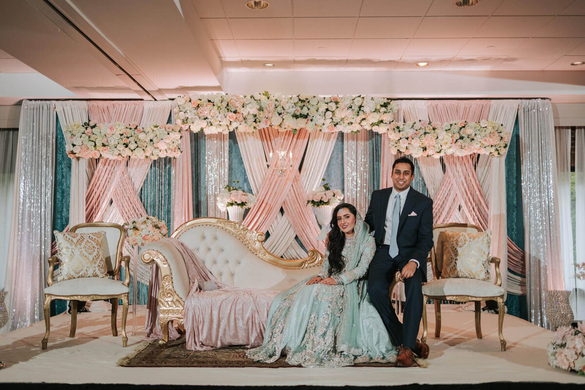 A couple poses elegantly on a floral-decorated stage with pastel tones at a Princeton, NJ wedding celebration.