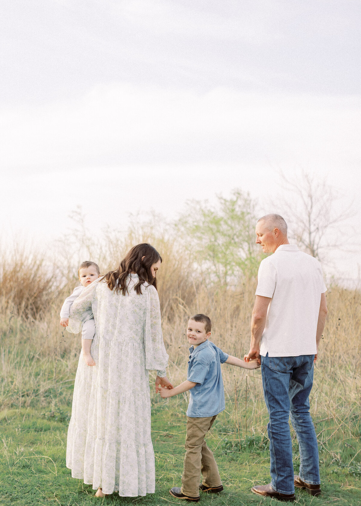 mom and dad holds hands with young son in the middle, mom holds baby on hip