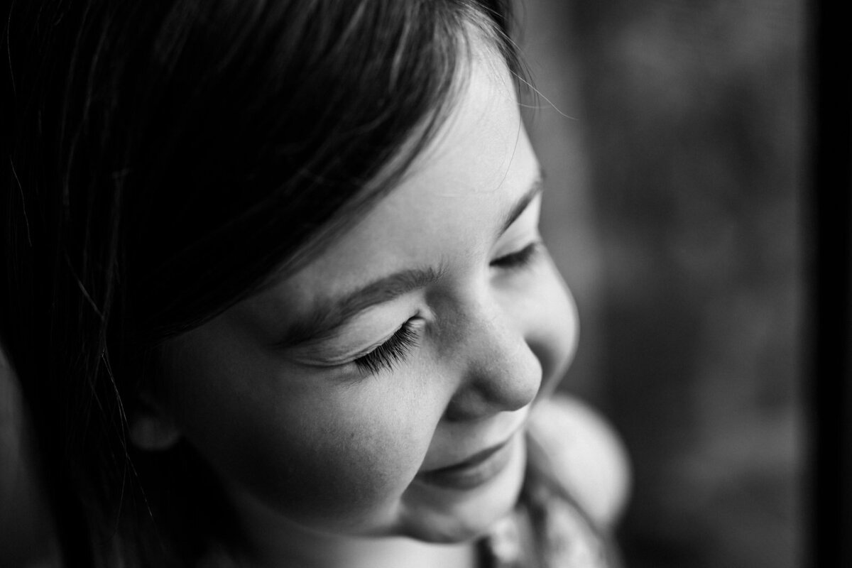 close up of girl smiling with eyes closed next to a window at home