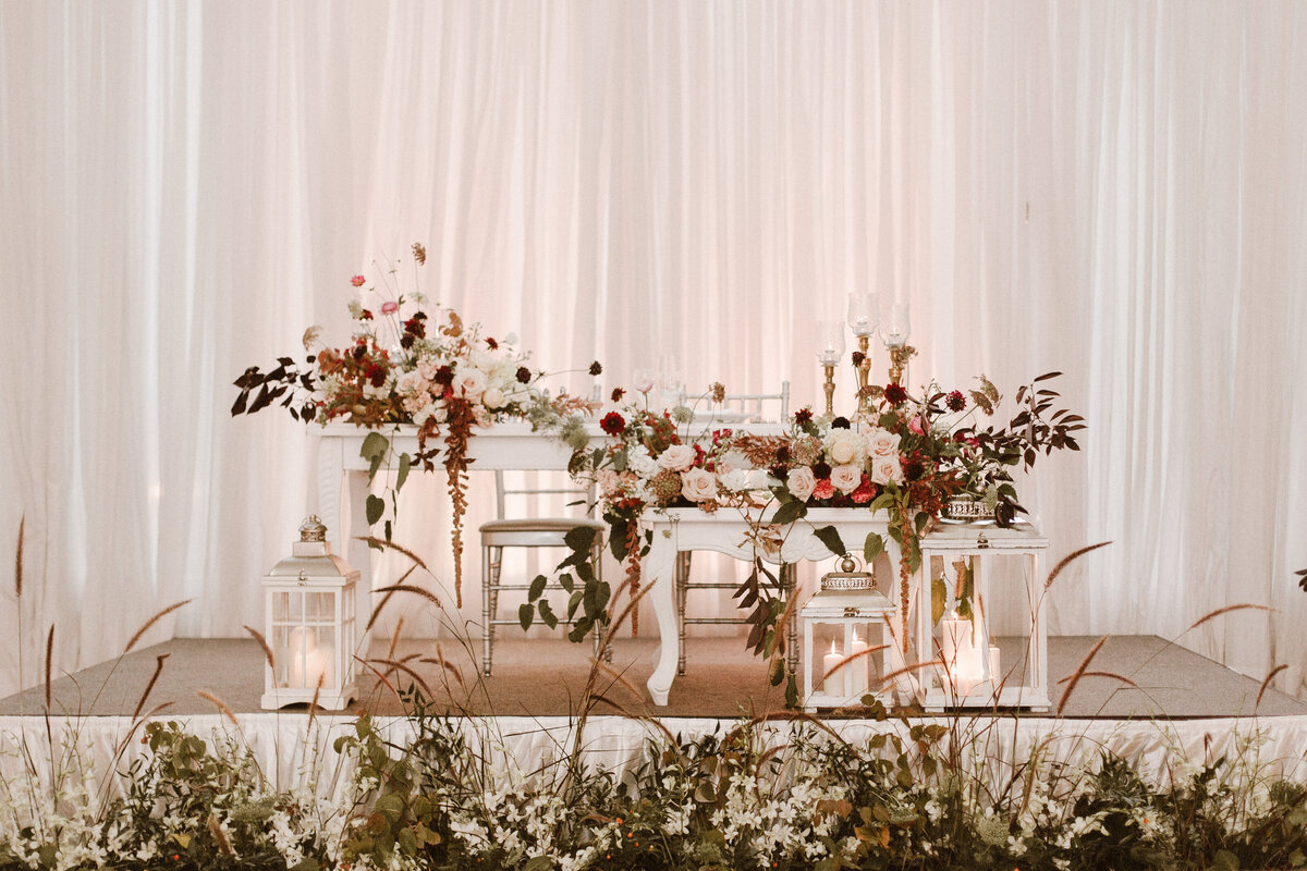 A sweetheart table at a Montreal wedding framed by garden flowers and a meadow of organic grasses.