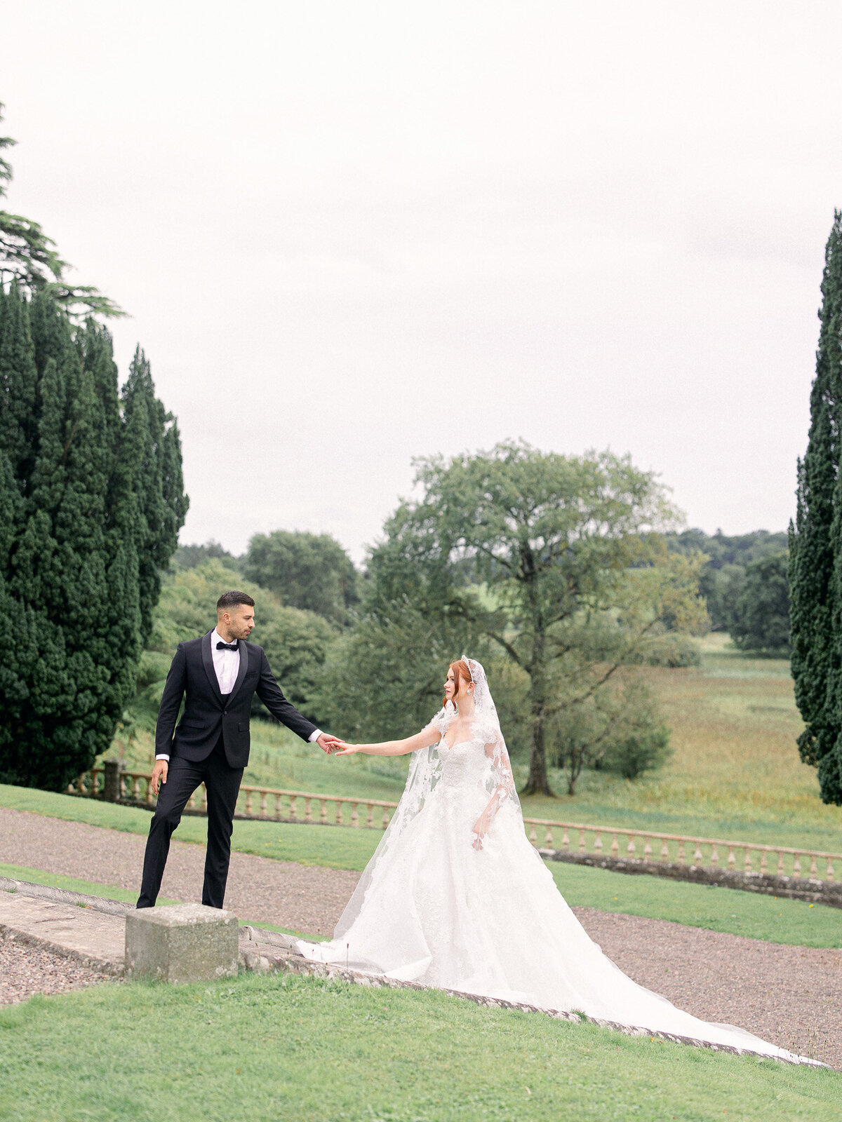 Groom in a black tux leads bride up stairs holding hands