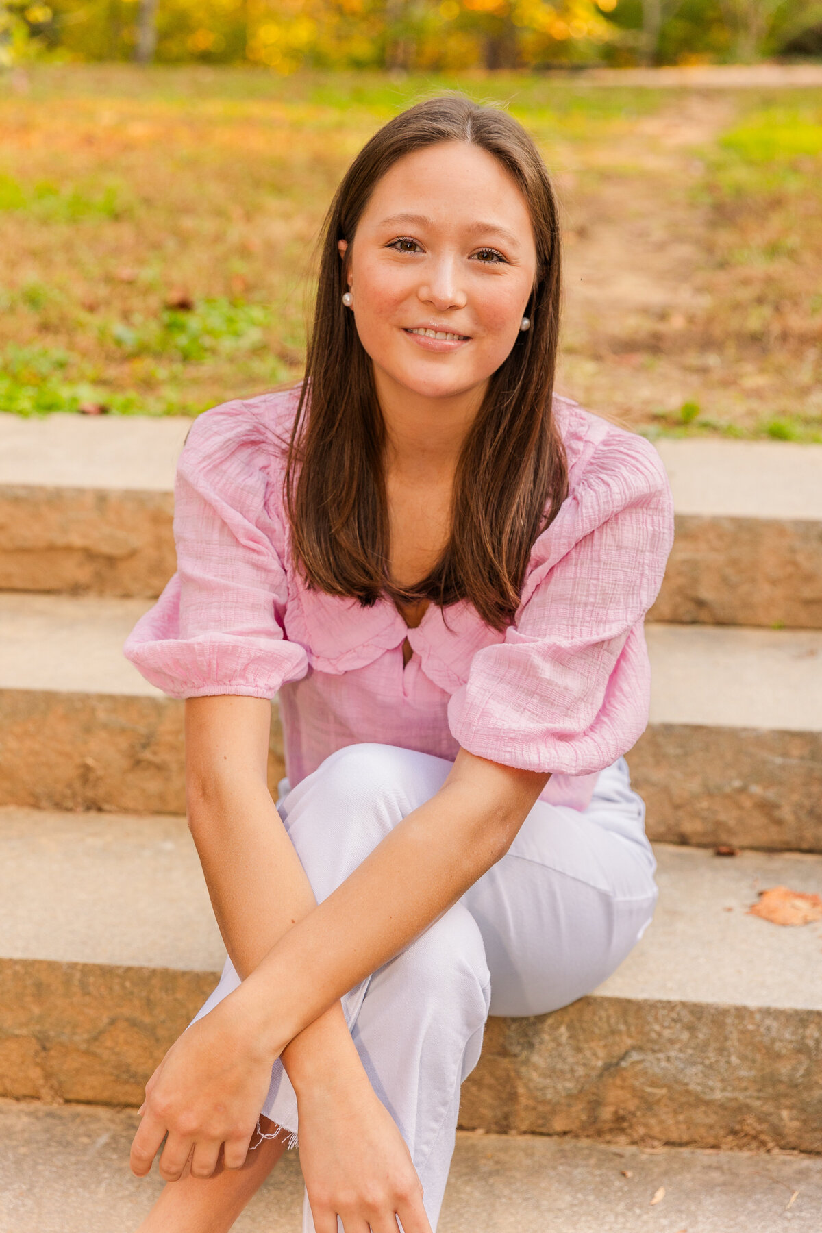young woman sitting on a park stairs legs crossed and hands over knees