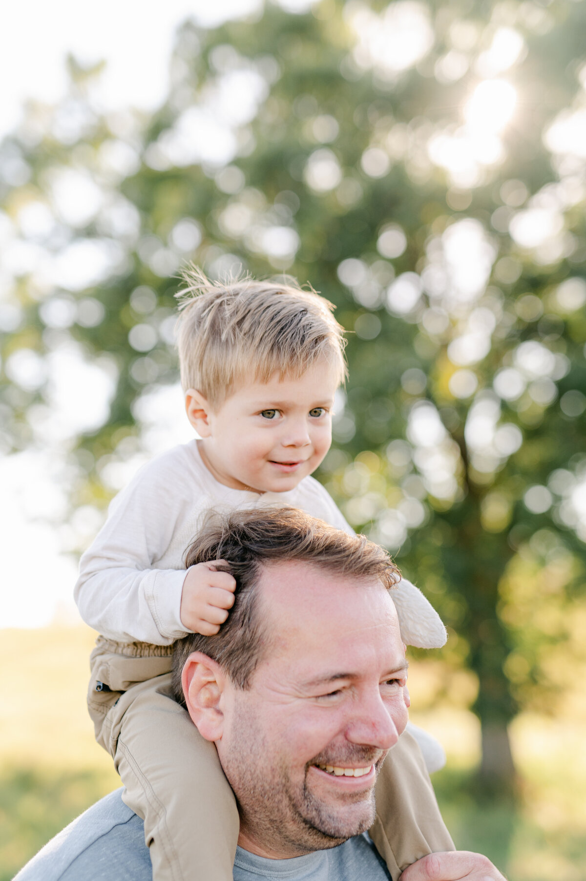 Little boy rides on dad's shoulders while the sun shines in the background