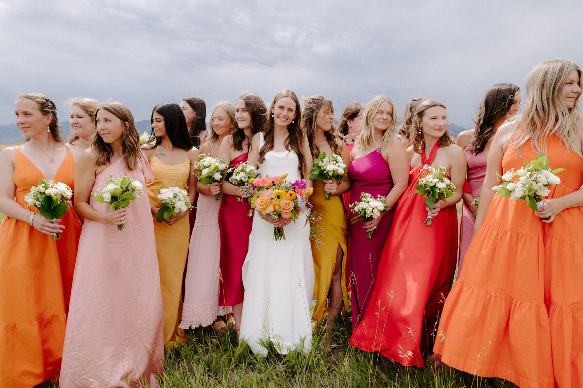 Bridesmaids in colorful dresses stand in field