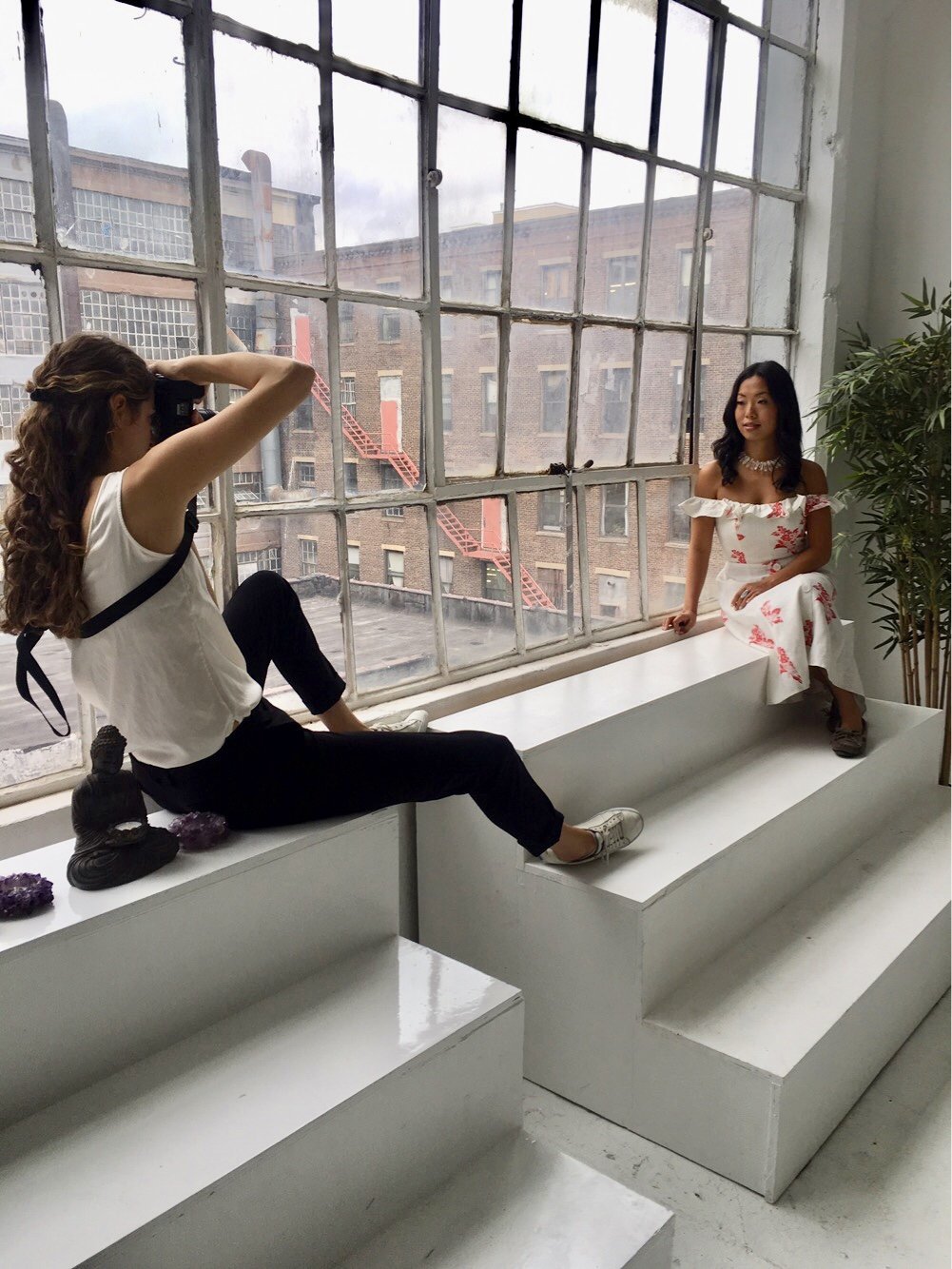 Laura Volpacchio photographs holistic wellness entrepreneur as she poses by a large industrial window  during a branding photography session in LIC, Queens