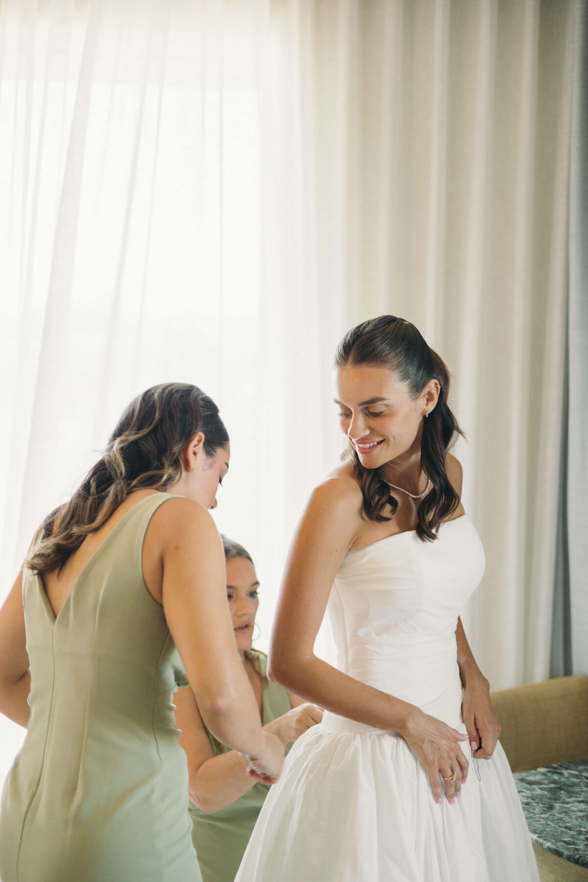 Bride smiling while bridesmaid adjusts wedding gown

