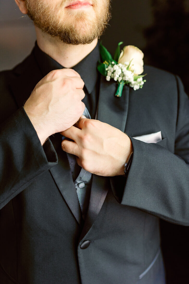 Portrait of the groom straightening his tie during groom prep photos.