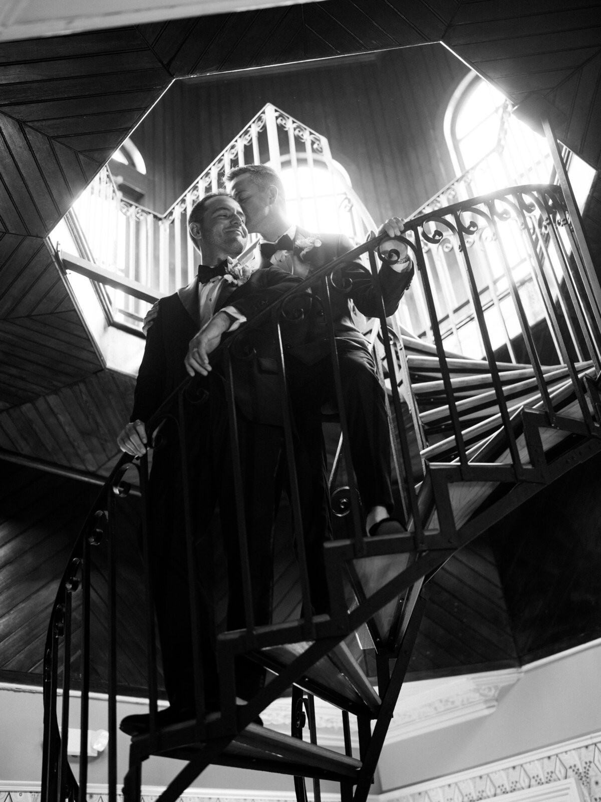 An artistic photograph of a couple embracing passionately on a spiral staircase, illustrating romance and elegance amidst a stunning architectural backdrop.