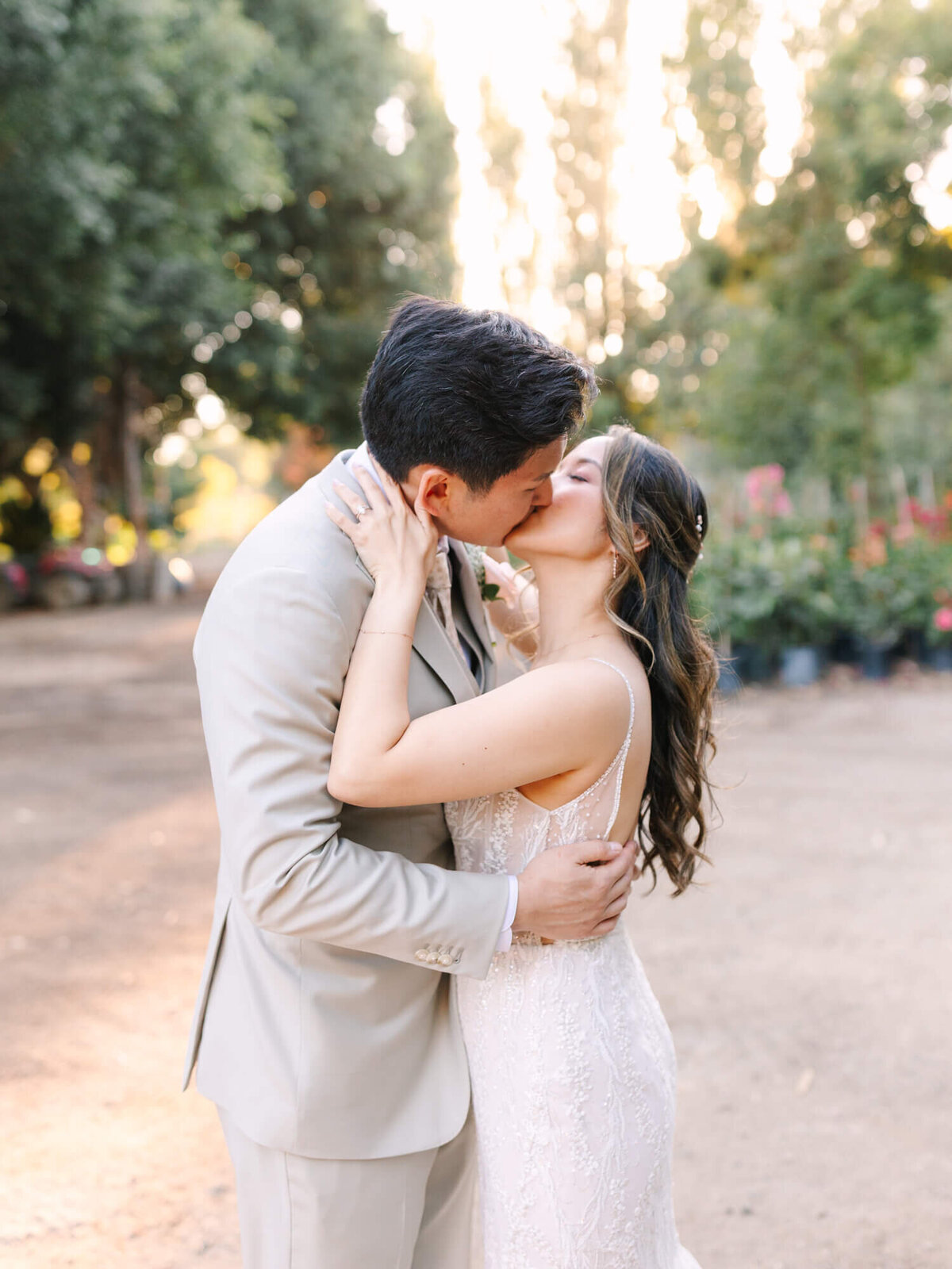 A couple kisses in a garden at Hartley Botanica. Sunlight filters through trees, creating a romantic atmosphere.