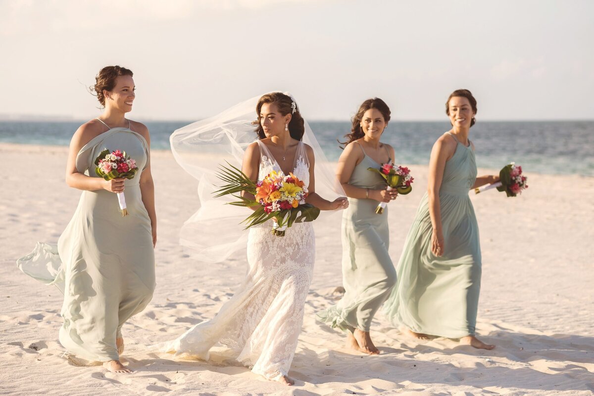 Bride and bridesmaids walking on beach after wedding in Cancun.