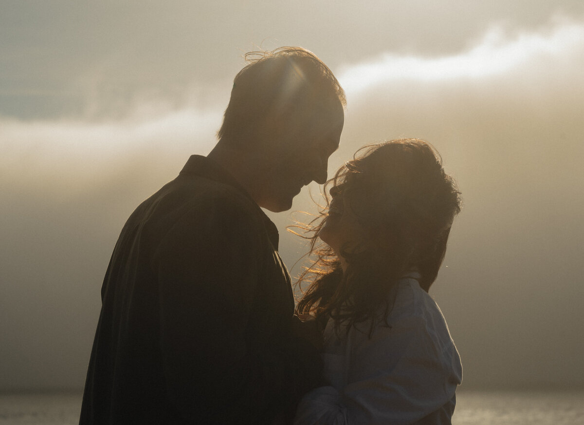 intimate, windswept moment of engaged couple smiling together on the sandy Oregon Coast