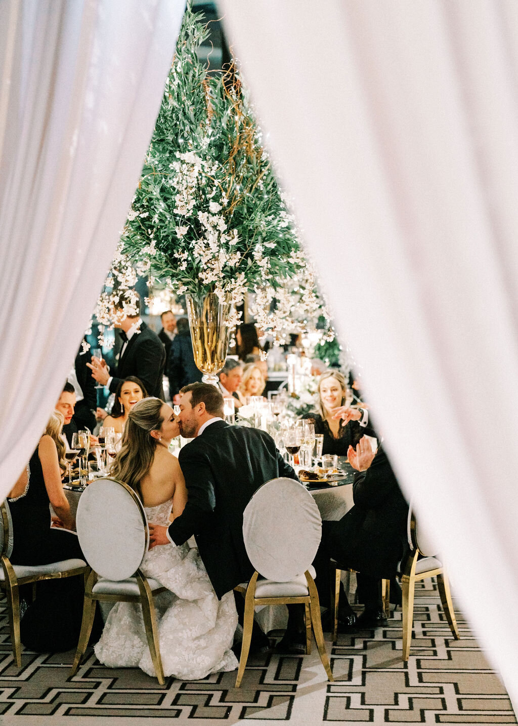 The bride and groom sharing a kiss at the table through the curtains. 