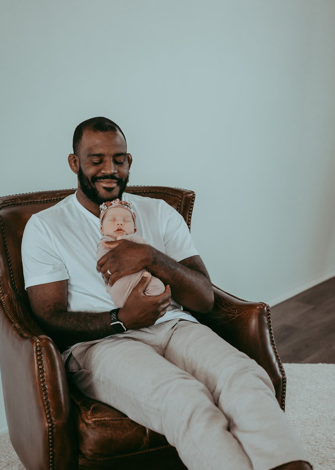 father reclines in leather chair while infant lays on his chest