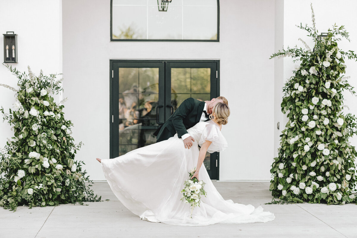 Bride and groom kissing in front of the doors of Sparrow Lane Events, a sophisticated and romantic wedding venue in Spruce Grove, AB, featured on the Brontë Bride Vendor Guide.