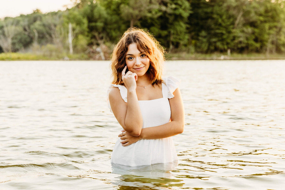 beautiful senior girl in a white dress posing in the water during her senior photo session