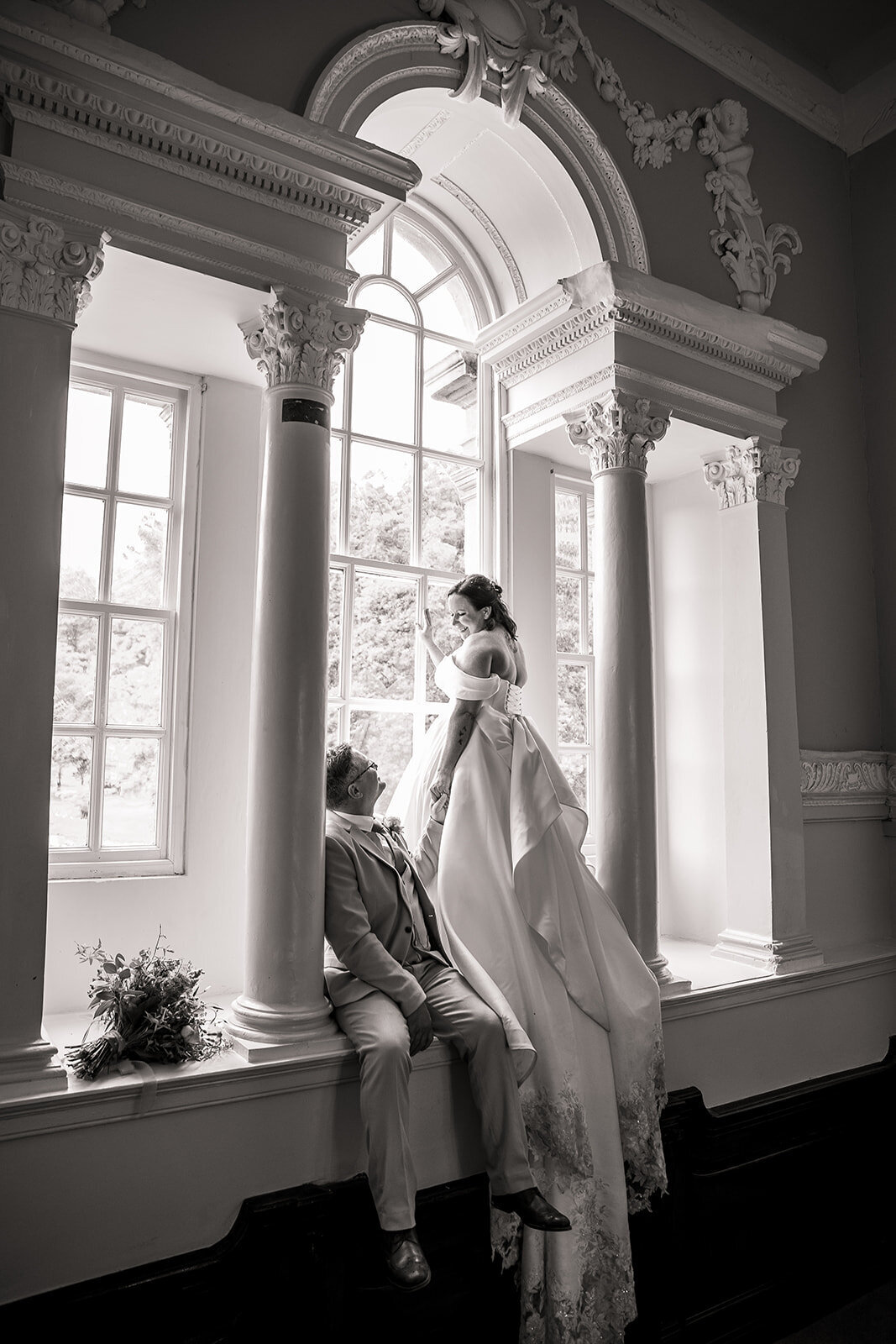 Bride stands in the window with her flowing wedding dress trailing to the floor