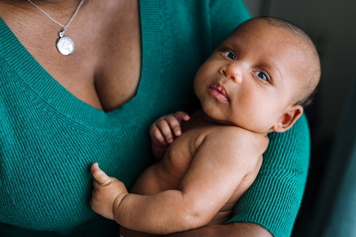 mom in green sweater holding newborn with no shirt and eyes open