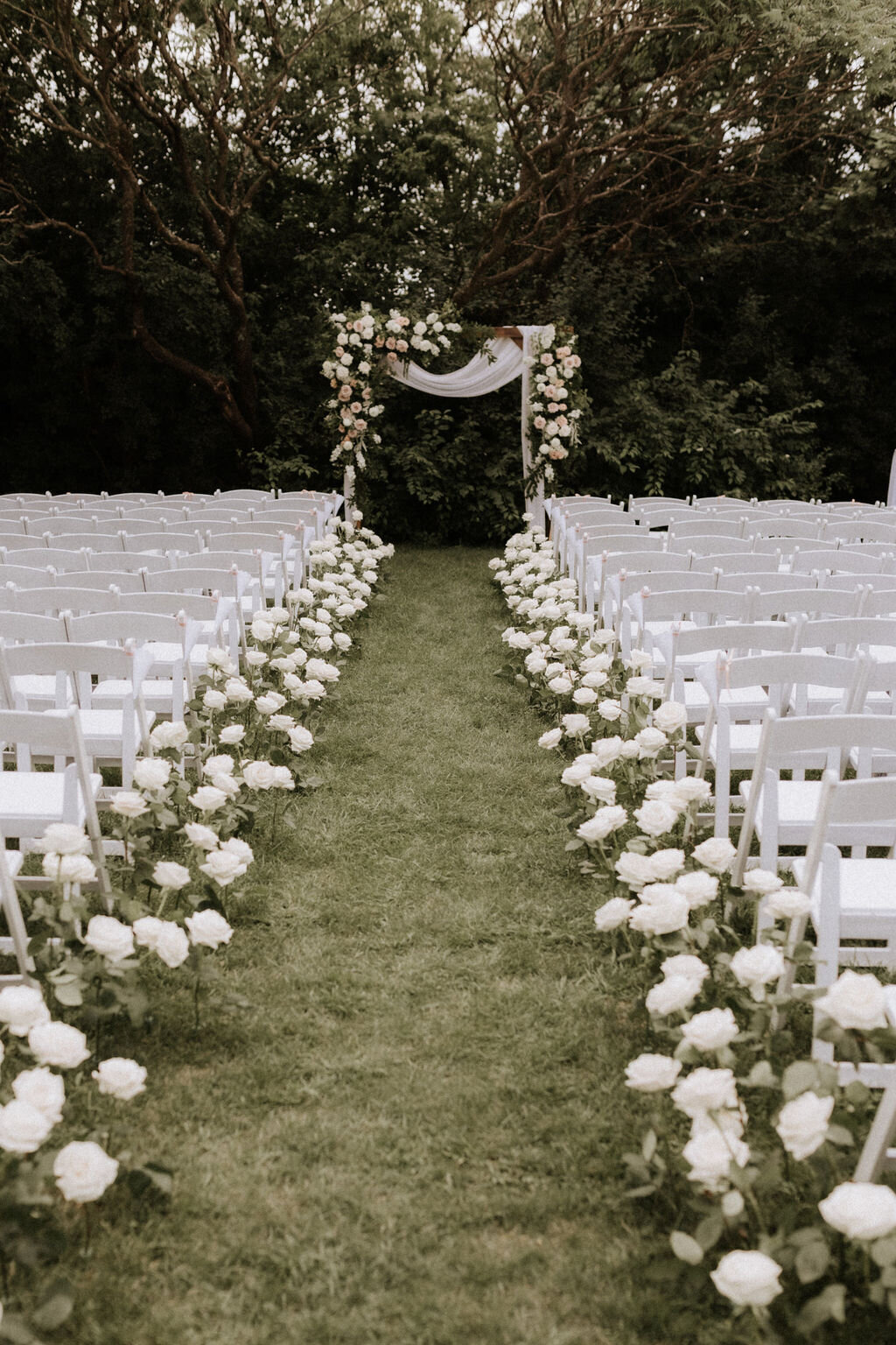 An aisle decorated with white roses for a wedding ceremony at Chapiteau Cardinal.