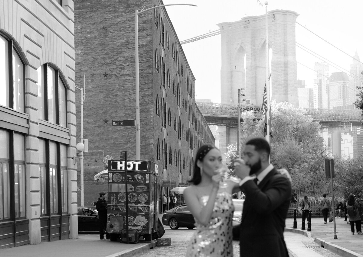 The couple embraces near the base of the Brooklyn Bridge, surrounded by the DUMBO neighborhood's textures.