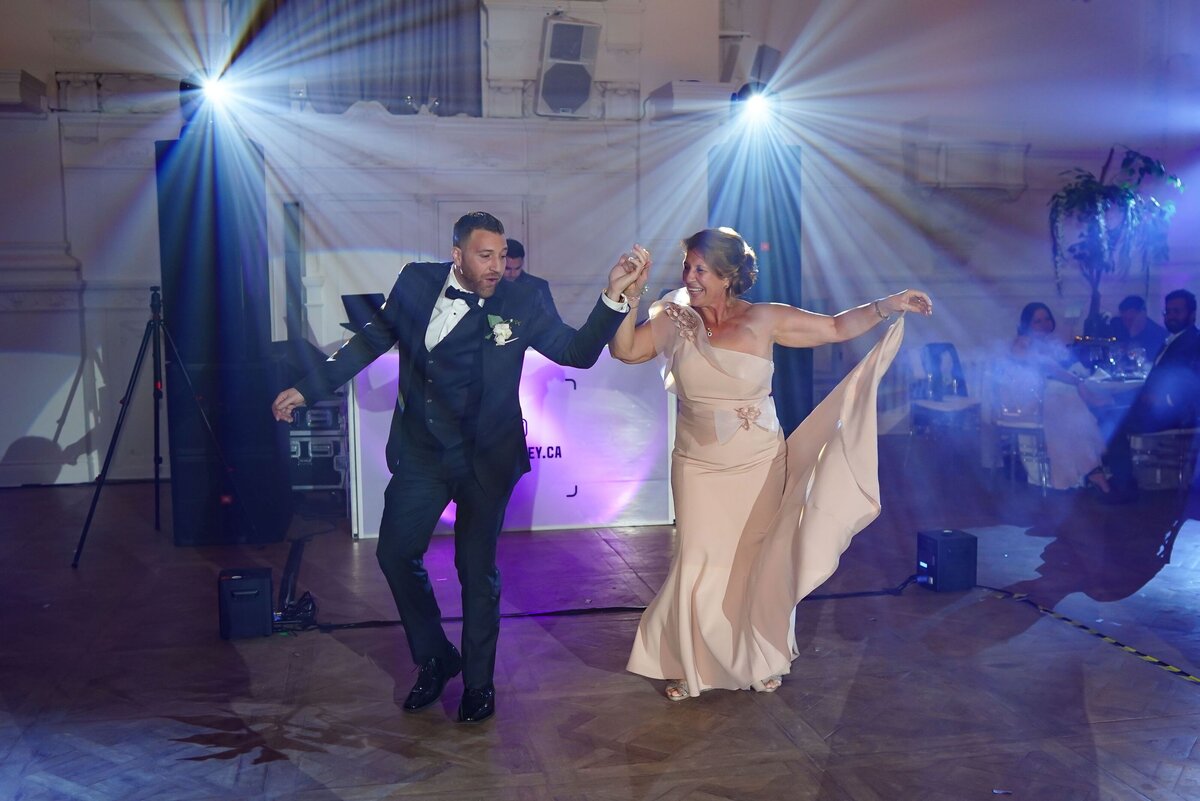 The groom and his mother engage in a lively traditional Greek dance during the wedding celebration, highlighting their cultural heritage and adding a festive touch to the event.