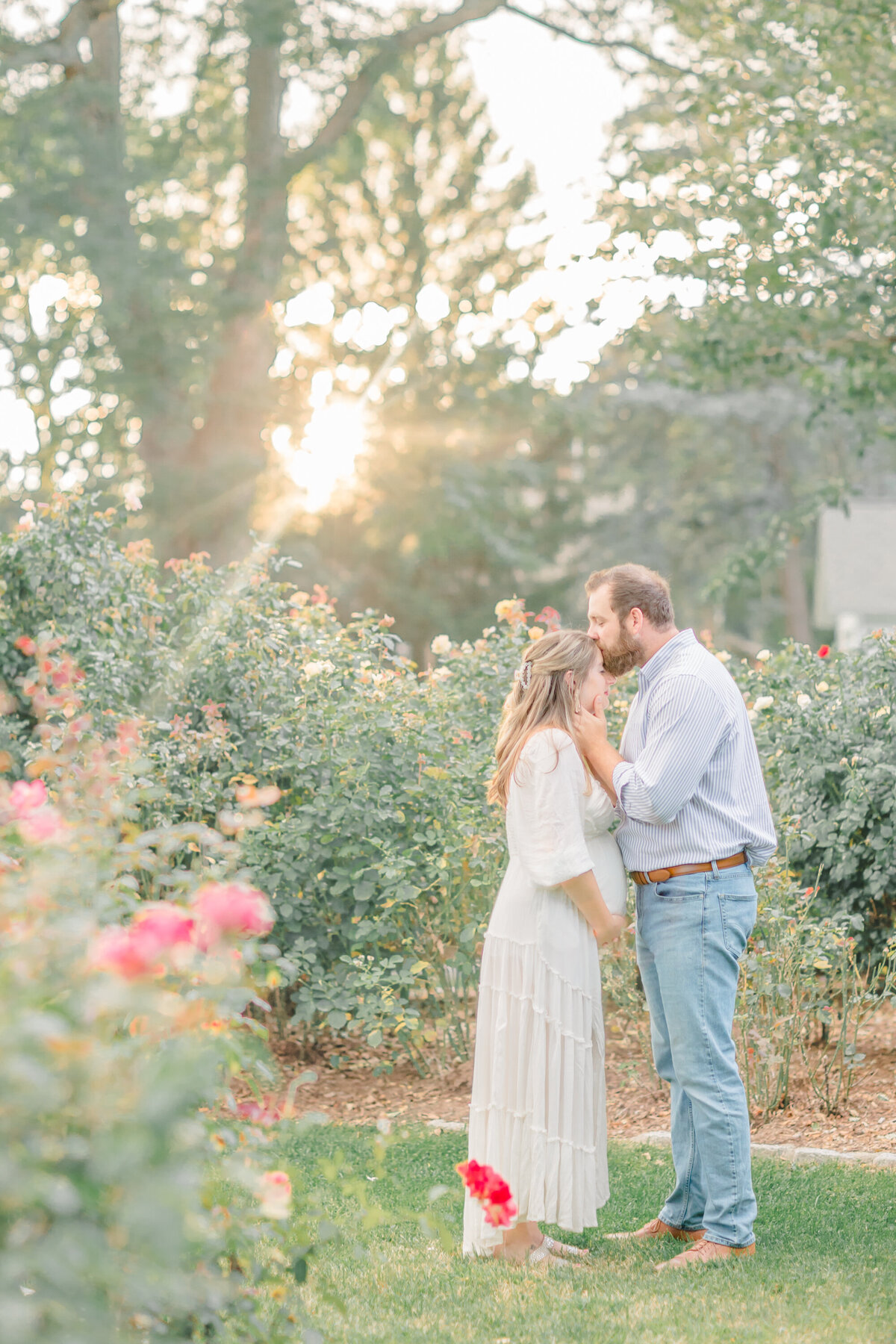 Couple embracing each other in a lush garden, with the expectant mother’s baby bump visible
