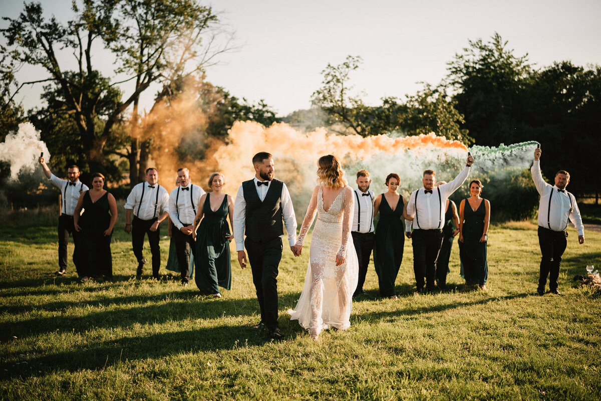 Bride and groom walking with bridal party at Lodge Farm House Hitchin with smoke bombs in a romantic outdoor wedding setting