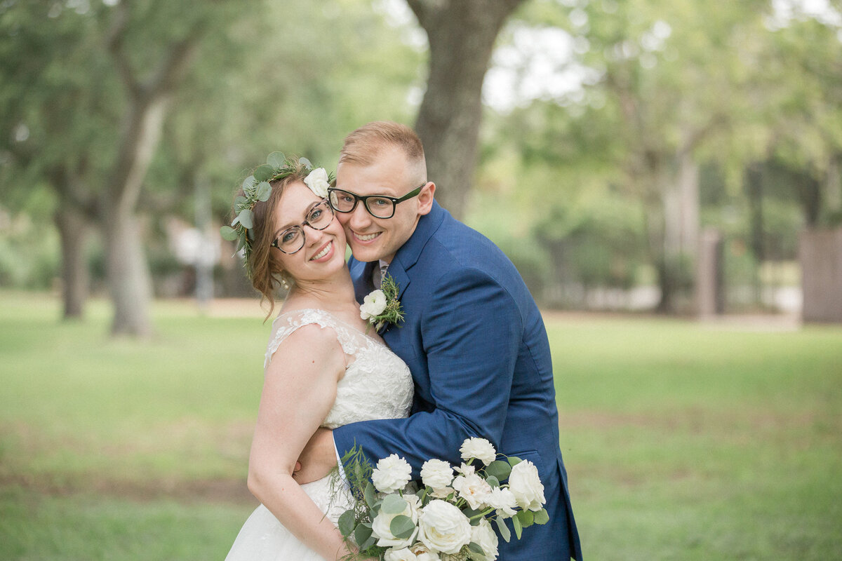 The bride and groom smile for the camera at the park on their wedding day