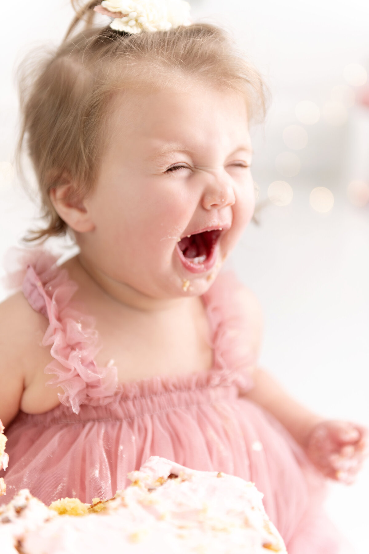 A toddler girl screams while smashing a cake in a pink dress