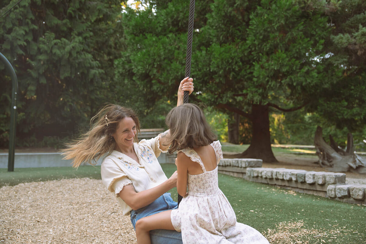mother riding on a zipline with daughter at the park