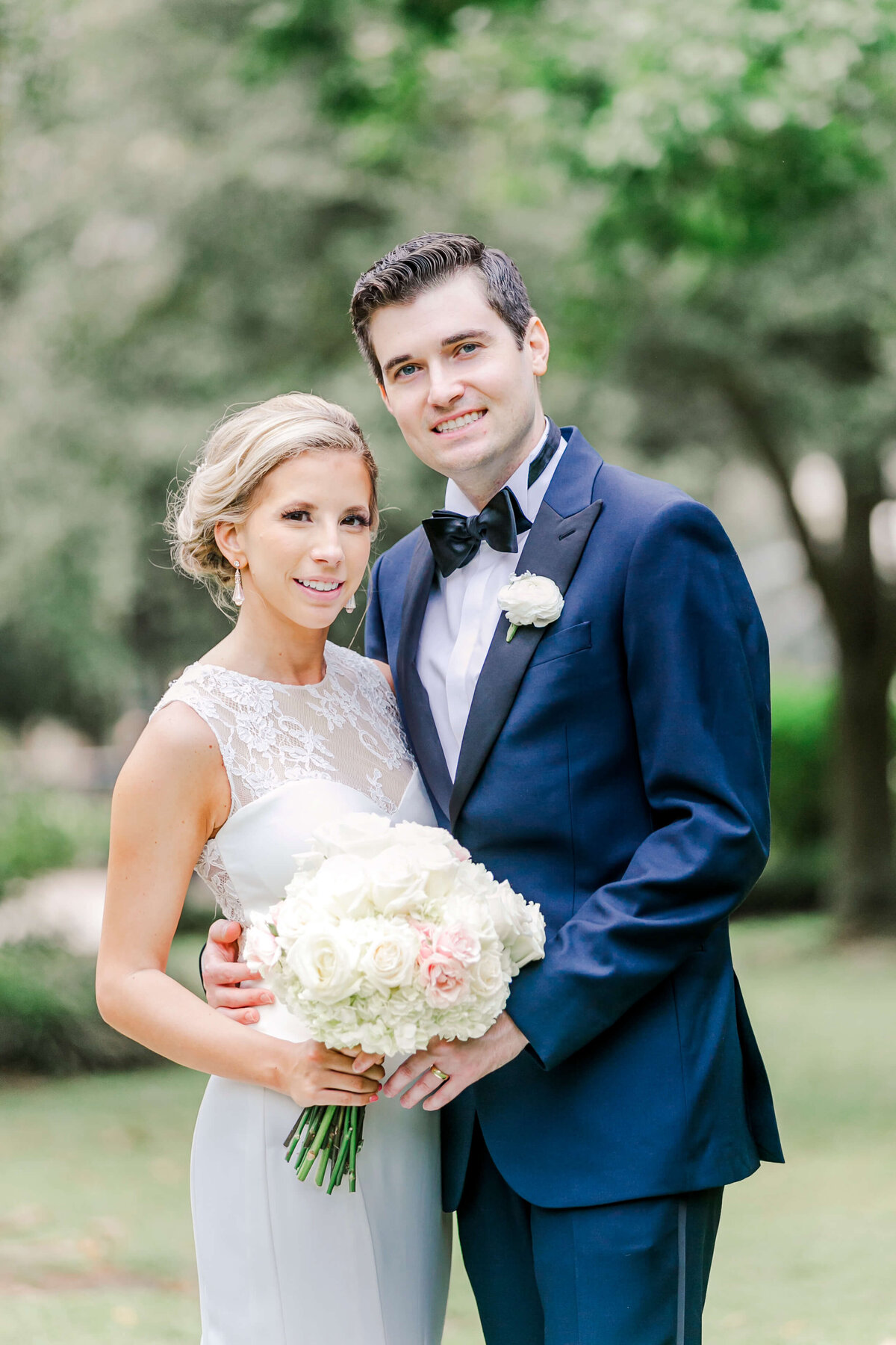 A groom in a blue tuxedo hugs his bride while standing in a lawn